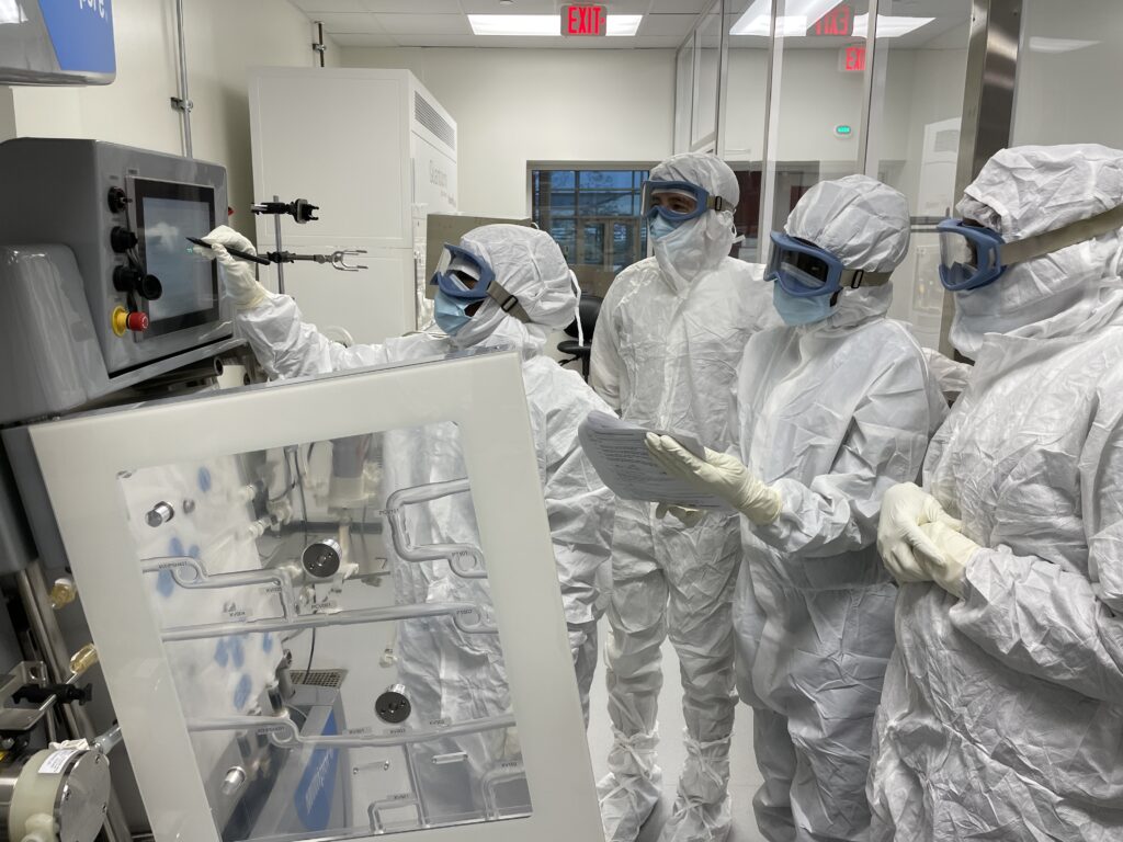Group of scientists in full lab gear examining samples in biomanufacturing lab