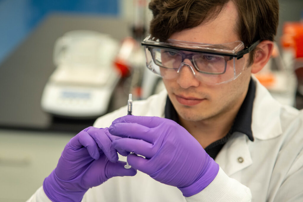 TRIBEC scientist wearing safety goggles examining syringe in biomanufacturing lab